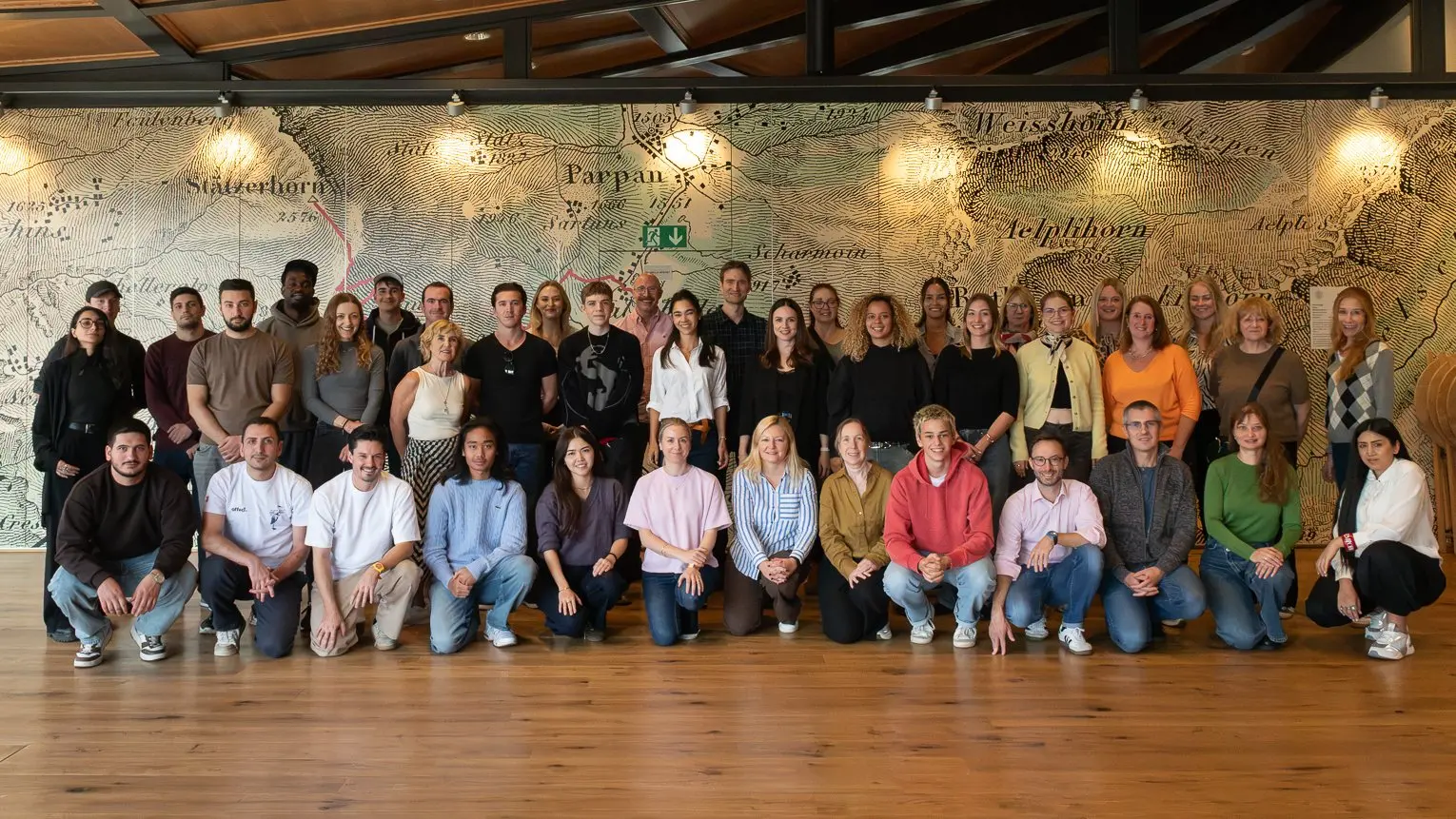 Das quinn Team, rund vierzig Menschen, in zwei Reihen in einem holzgetäfelten Saal vor einer grossen historischen Landkarte.